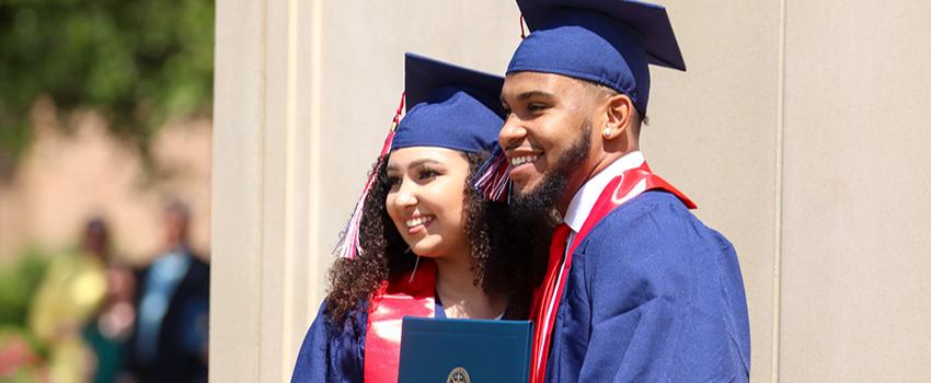 Two new graduates smiling holding diploma.